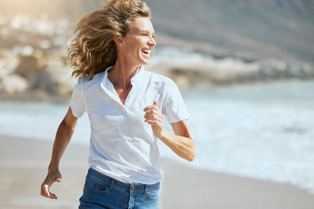Healthy Living by the Shore – Chiropractor Manahawkin NJ A smiling woman runs along the beach, embodying energy, movement, and freedom from pain through balanced wellness – Chiropractor Manahawkin NJ.