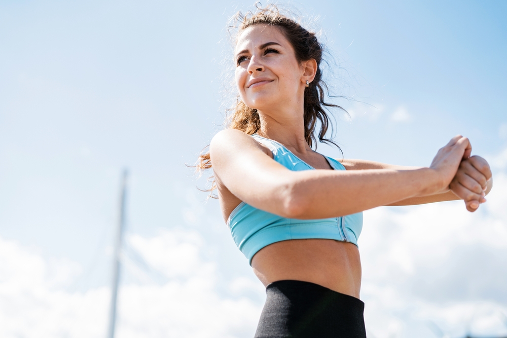 Posture and Strength Training – Chiropractor Manahawkin NJ A young woman in fitness gear stretches under a bright sky, symbolizing improved flexibility and alignment through chiropractic wellness – Chiropractor Manahawkin NJ.