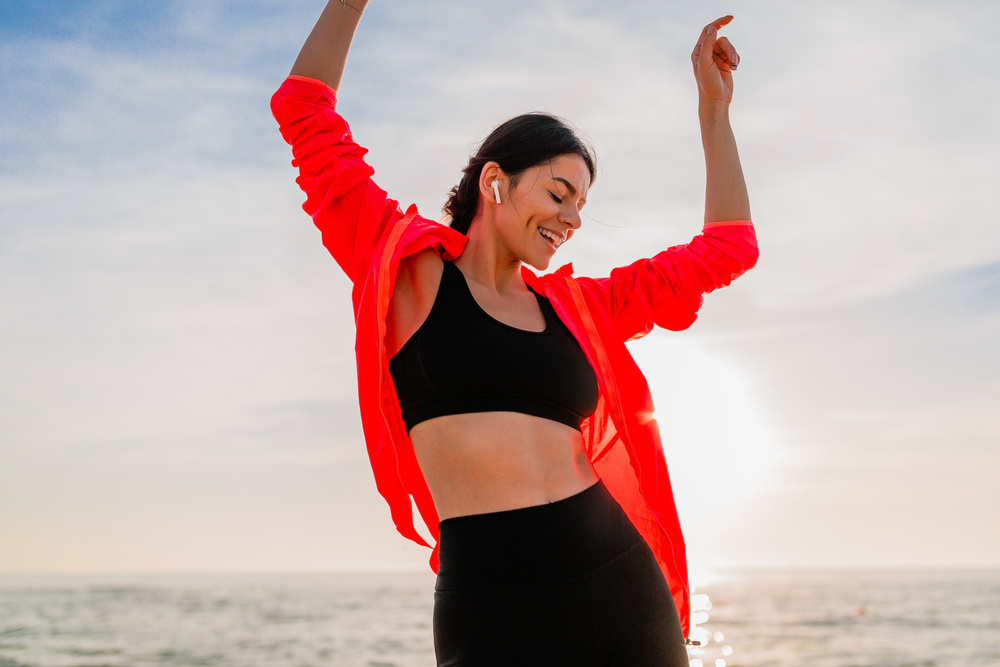 Active Beach Lifestyle – Chiropractor Manahawkin NJ A woman stretches joyfully at the beach in athletic wear, showcasing a healthy and active lifestyle inspired by chiropractic care – Chiropractor Manahawkin NJ.
